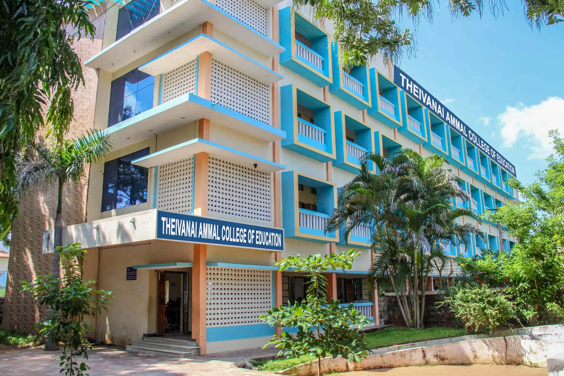 The college's four-storey building, painted cream and sky blue, with palm trees in front.