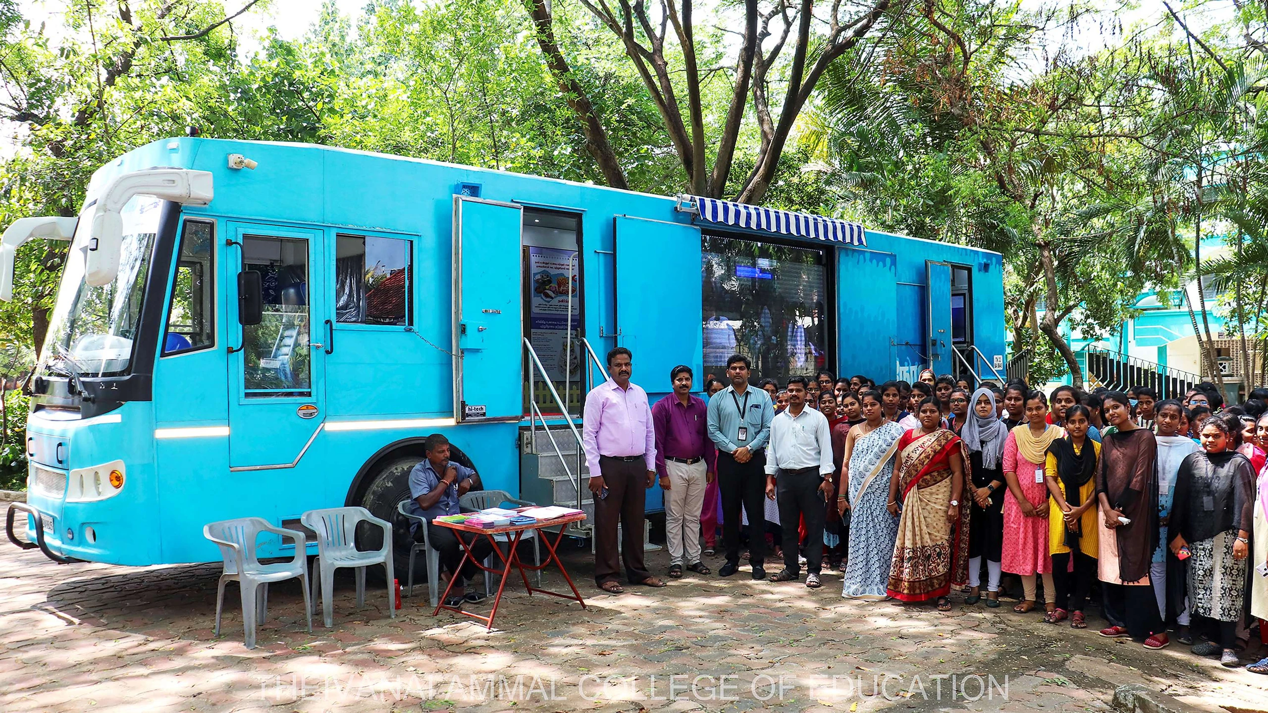 Students and staff stand in front of a blue Adyar Cancer Institute bus.