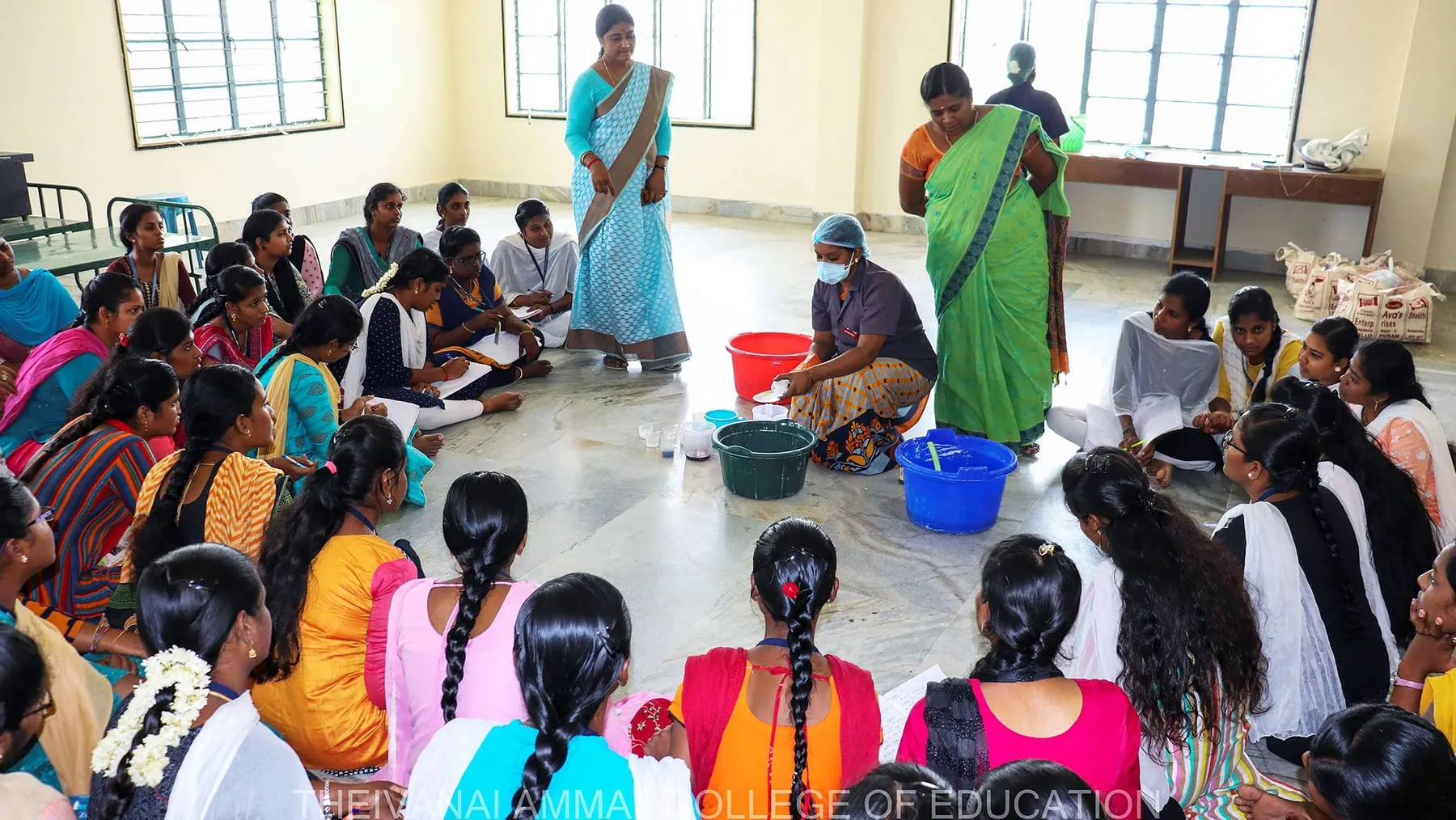 Students sit on the floor around bowls and buckets during a hands-on session.