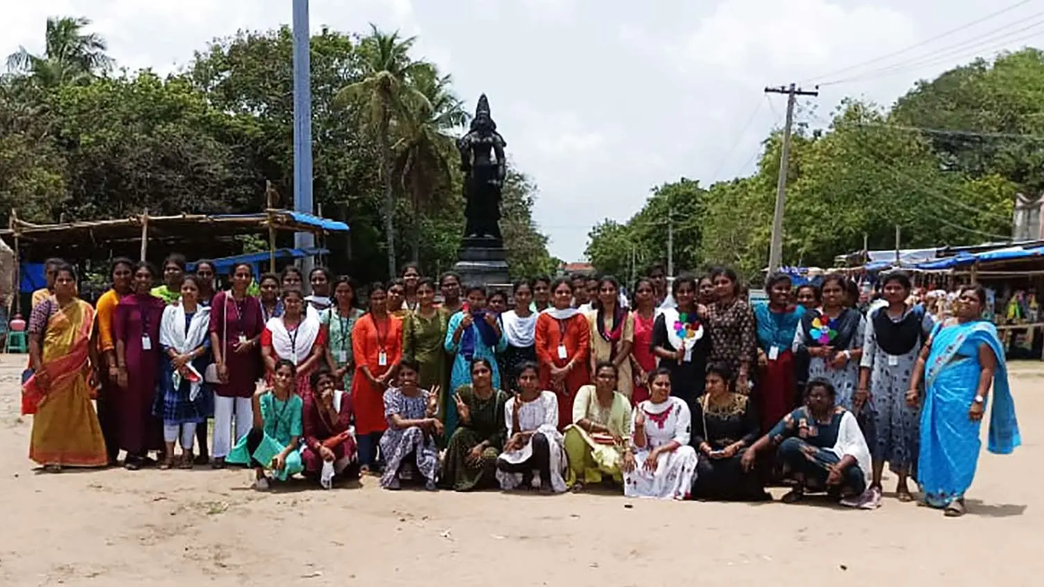 A large group of students poses in front of a statue at Poompuhar.